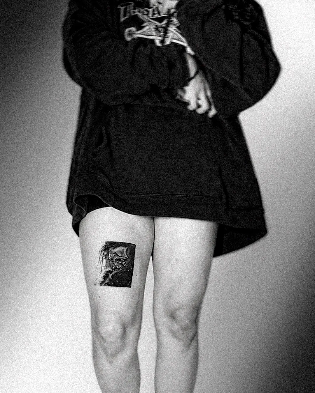 Black and grey framed portrait tattoo of a brooding hooded figure on the thigh
