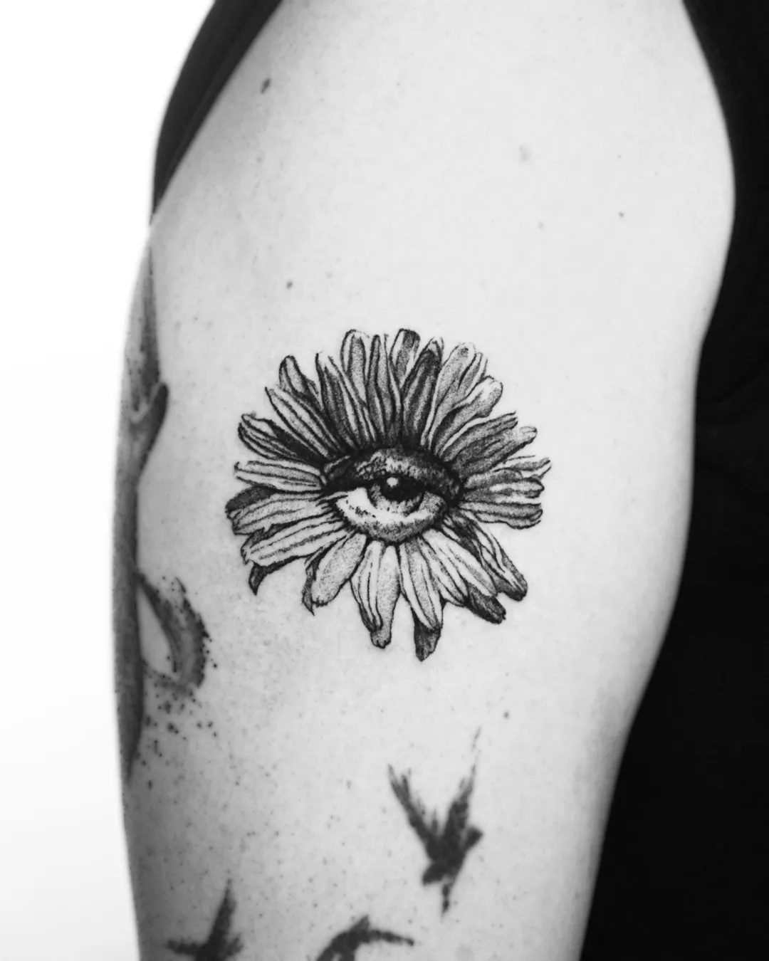 Black and grey dotwork daisy with a human eye at its center, upper arm