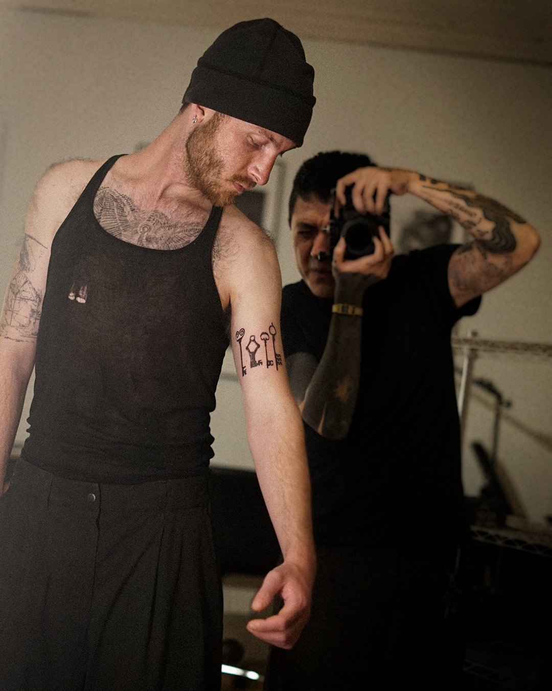 Behind-the-scenes editorial: Lalo photographs a subject wearing the Keys tattoo on the upper arm, holding a camera up to the mirror
