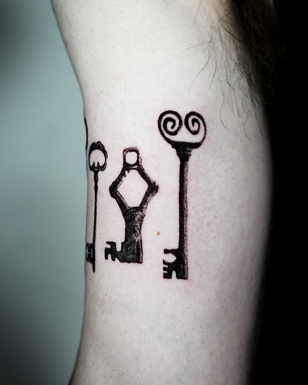 Fine line tattoo on inner upper arm: three antique keys of different heights and patterns, drawn in clean black ink