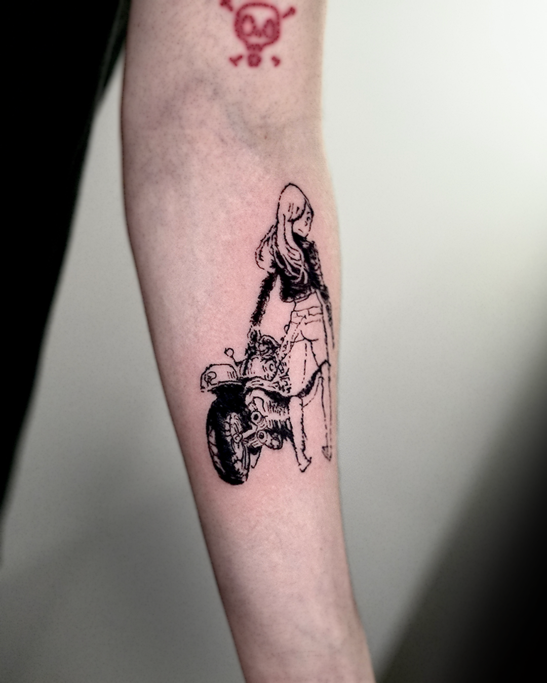 Sketch-style tattoo on inner forearm: a long-haired girl standing next to a vintage motorbike, drawn in delicate woodcut linework