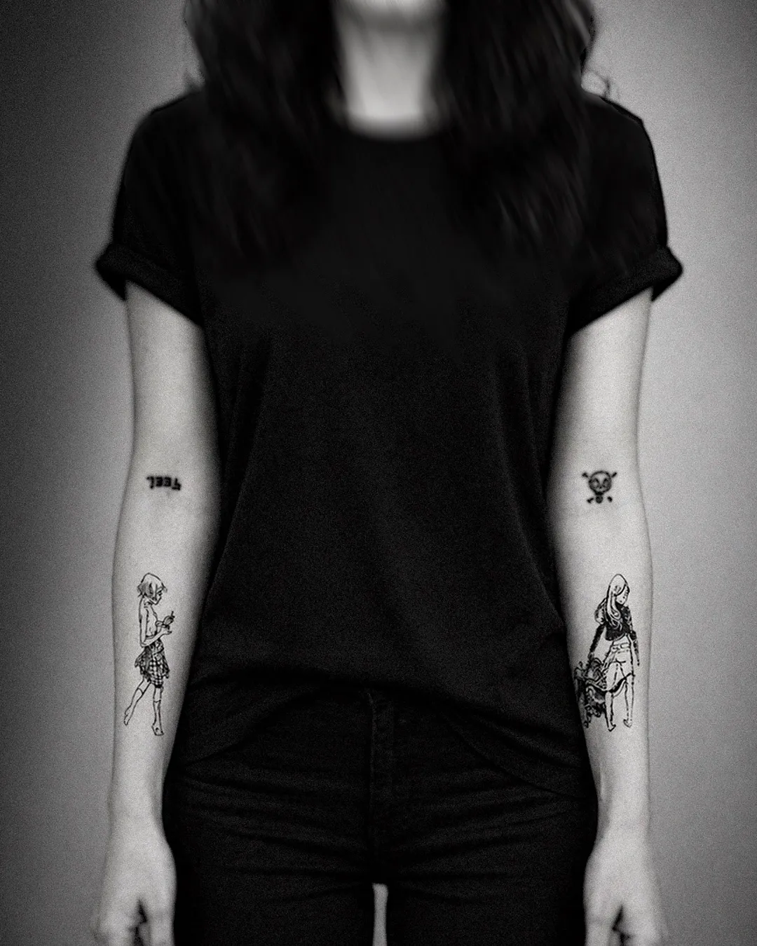 Two manga-style line figures tattooed on both forearms