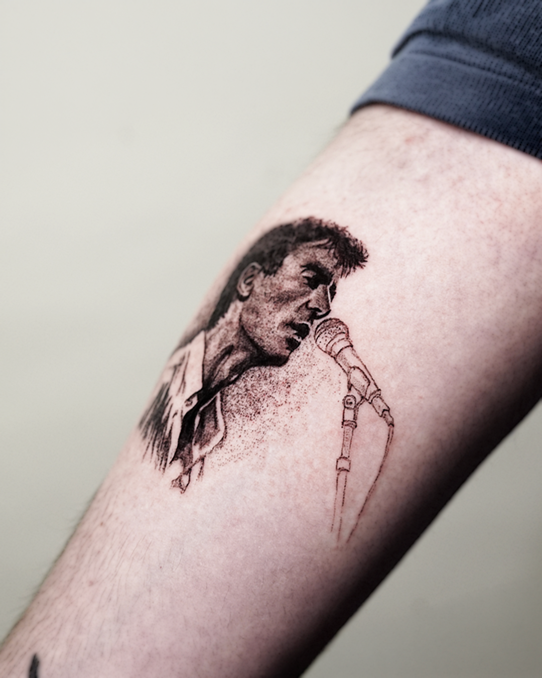 Close-up of the Talking Heads tattoo: fine line black and grey portrait of David Byrne singing into a microphone