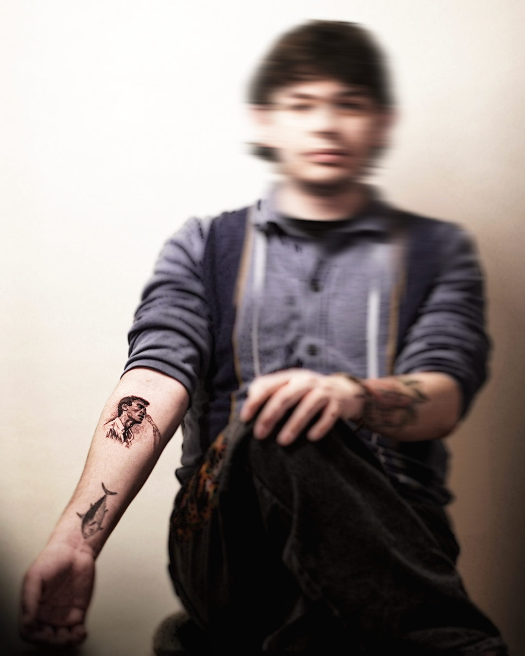 Cinematic portrait of a young man in overalls with a small black-and-grey tattoo visible on his forearm